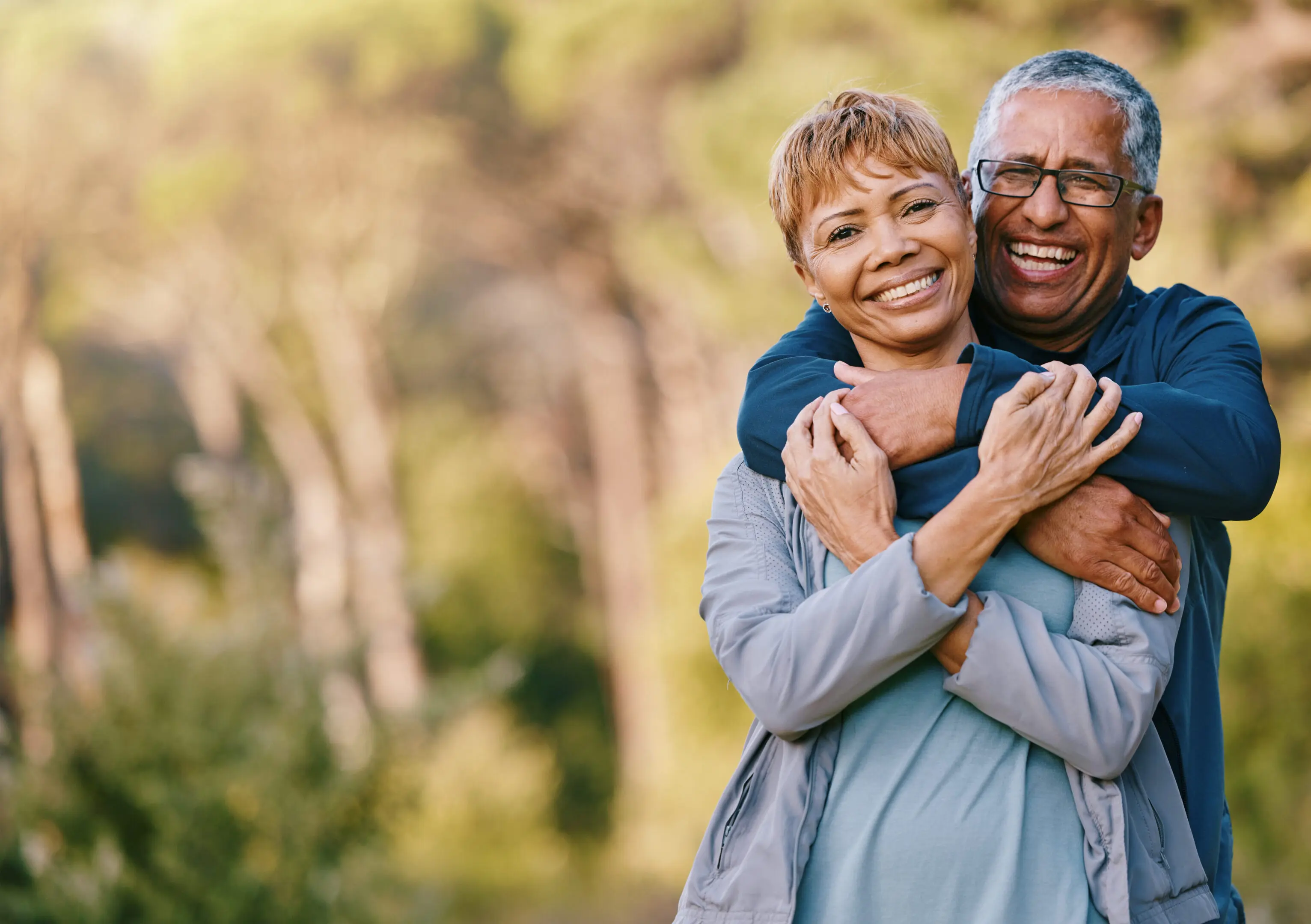 A man and woman hugging in the woods.