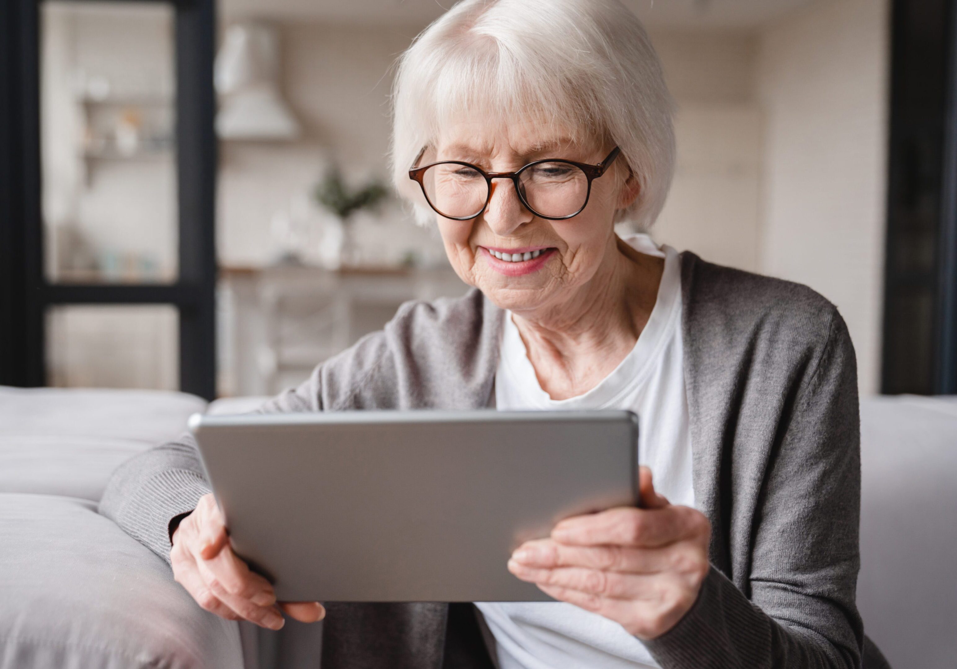 Caucasian beautiful old elderly senior woman lady grandmother using tablet for surfing social media, e-banking, e-commerce, checking pension, mortgage loan online at home A woman sitting on the couch looking at her tablet.