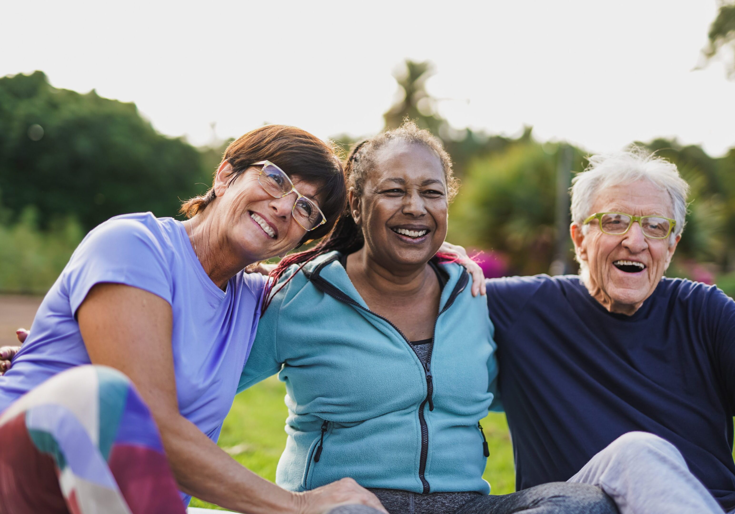 Happy elderly people having fun hugging each other outdoor after yoga lesson Three people are smiling for a picture.