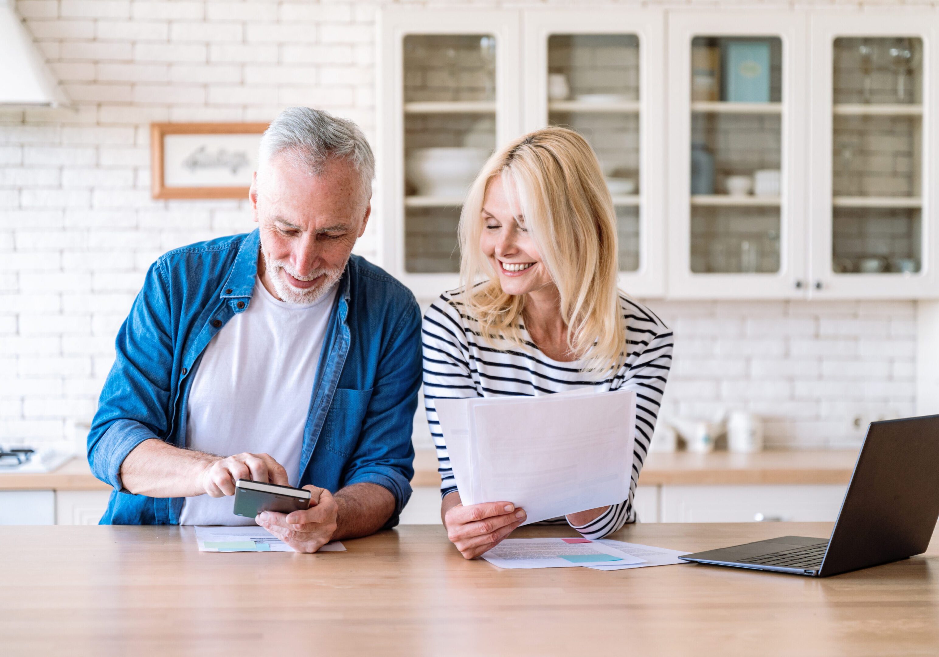 Happy mature family couple managing household budget together A man and woman sitting at a table looking at papers.