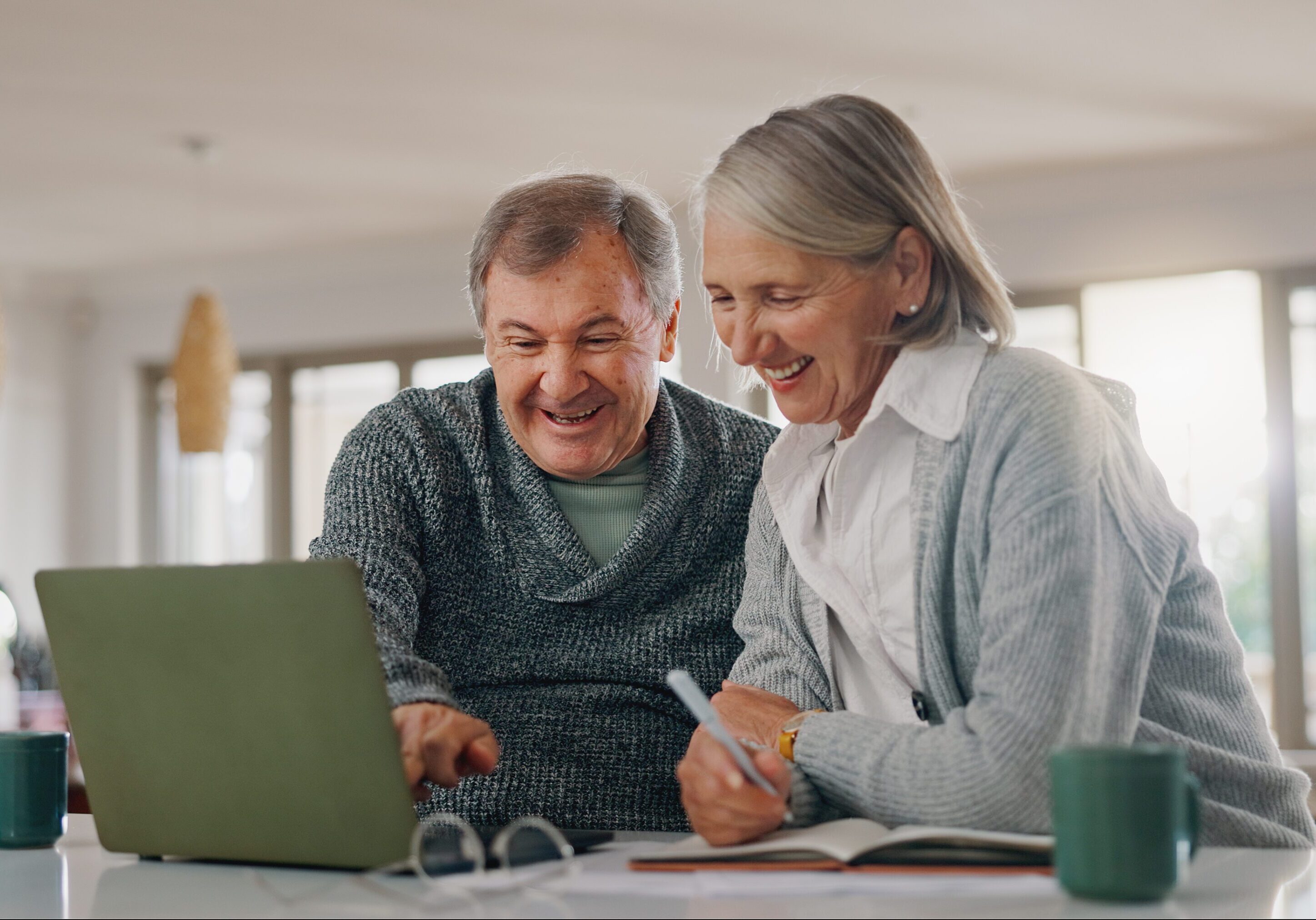Senior man, woman and laptop with paperwork, writing and happy with profit, investment and retirement. Elderly people, couple and computer with documents for pension, review and financial freedom A man and woman looking at a laptop