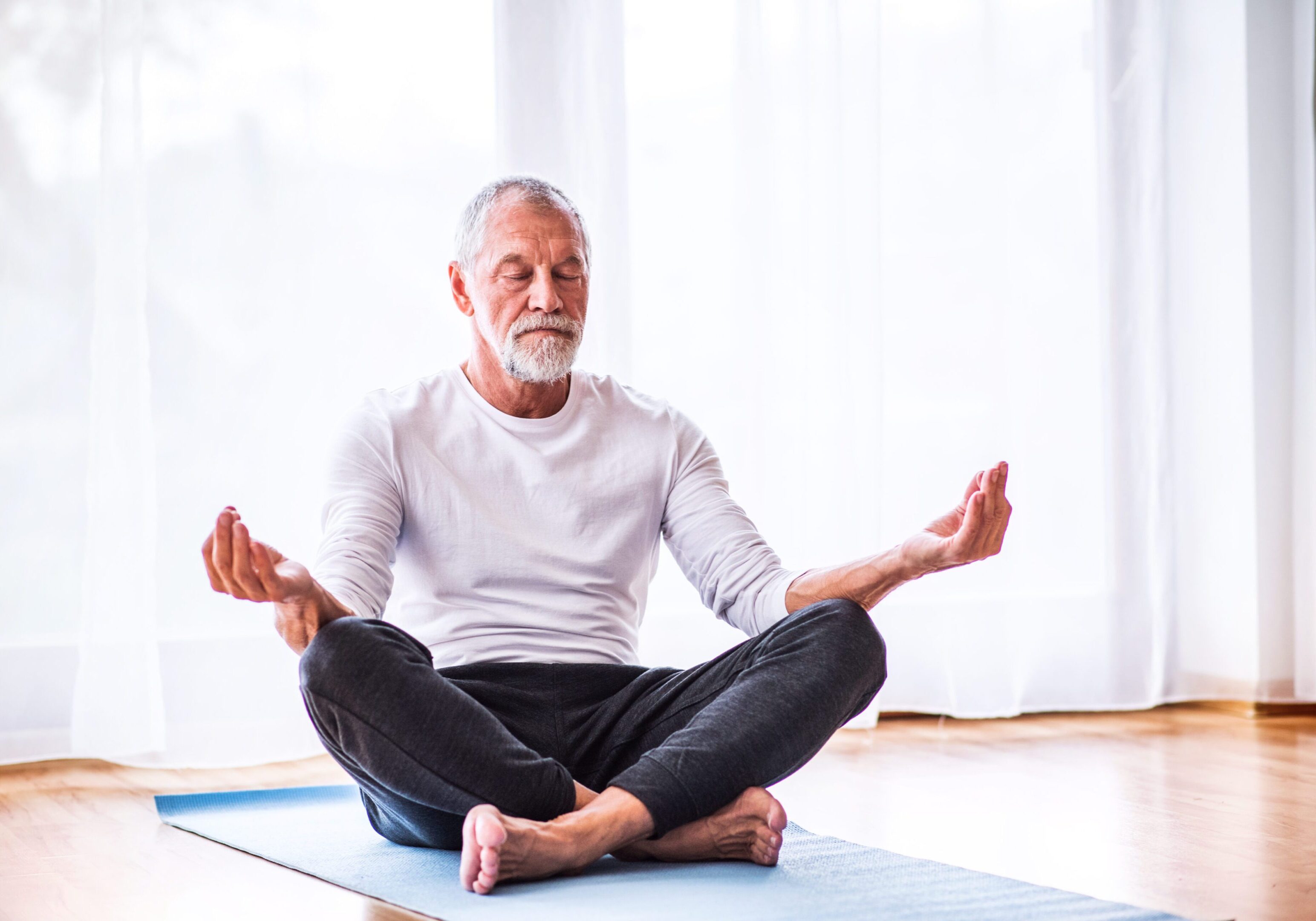 Senior man meditating at home. A man sitting on the ground in a yoga pose.